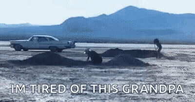 A Car Is Driving Down A Dirt Road Next To A Pile Of Dirt And Mountains . GIF