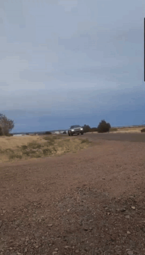 A Car Is Driving Down A Dirt Road With A Blue Sky In The Background GIF