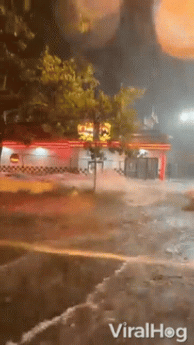 A Car Is Driving Down A Flooded Street At Night In Front Of A Restaurant . GIF