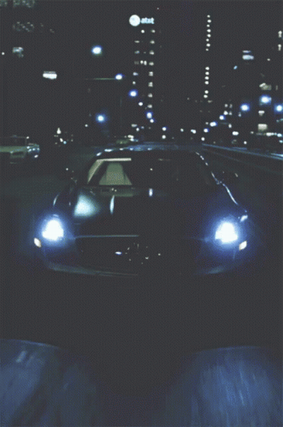 A Car Is Driving Down A Highway At Night With An At & T Building Behind It GIF