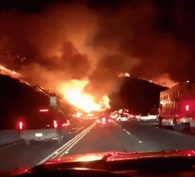 A Car Is Driving Down A Highway In Front Of A Huge Fire GIF