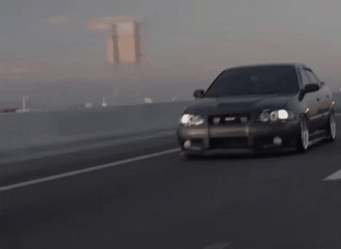A Car Is Driving Down A Highway With A Bridge Behind It GIF