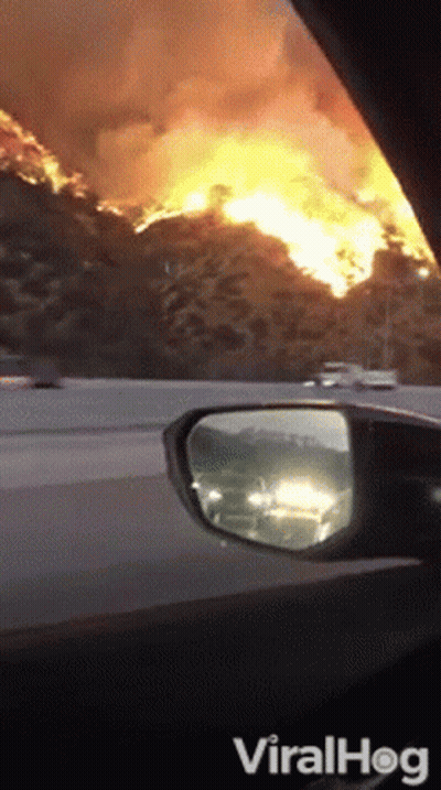 A Car Is Driving Down A Highway With A Large Fire In The Distance GIF