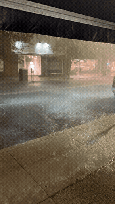 A Car Is Driving Down A Rainy Street In Front Of A Store GIF