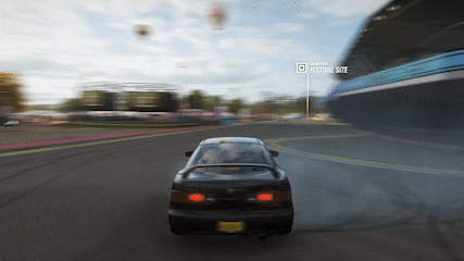 A Car Is Driving Down A Road In Front Of A Festival Site GIF