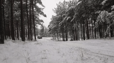 A Car Is Driving Down A Snowy Road In The Woods . GIF