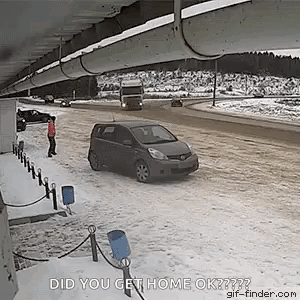 A Car Is Driving Down A Snowy Road Under A Bridge And A Man Is Standing On The Side Of The Road . GIF