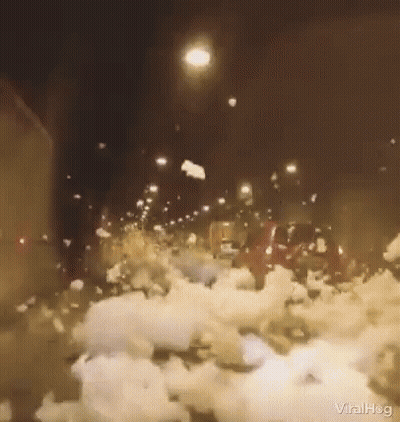 A Car Is Driving Down A Snowy Street At Night With A Lot Of Snow On The Ground . GIF