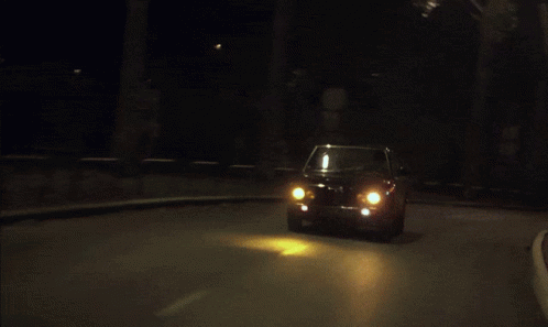 A Car Is Driving Down A Street At Night With The Lights On GIF