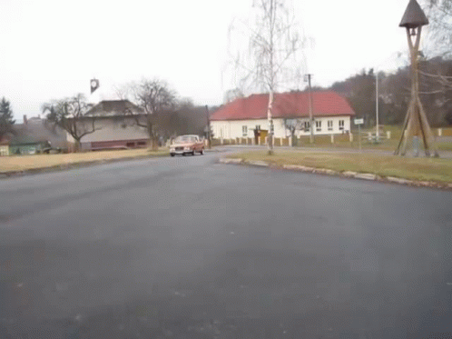 A Car Is Driving Down A Street In Front Of A Bell Tower GIF