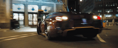 A Car Is Driving Down A Street With A Building In The Background That Has A Sign That Says No Parking GIF