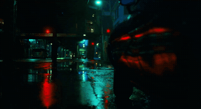 A Car Is Driving Down A Wet Street With A Red Light In The Background GIF