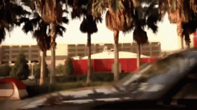 A Car Is Driving Past A Tent And Palm Trees In Front Of A Building GIF