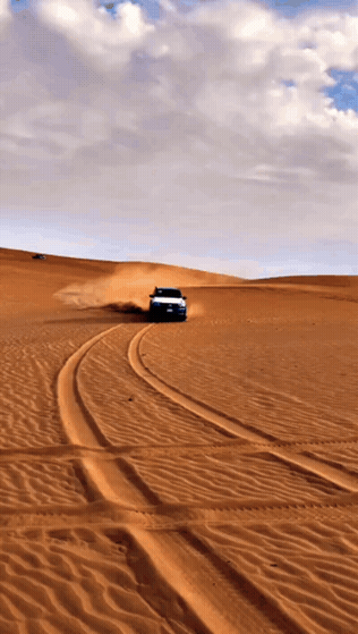 A Car Is Driving Through A Desert With A Cloudy Sky In The Background GIF