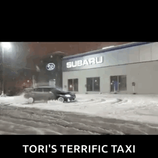 A Car Is Driving Through The Snow In Front Of A Subaru Car Dealership . GIF