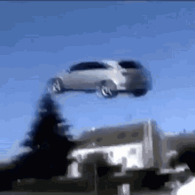 A Car Is Flying In The Air Over A House . GIF