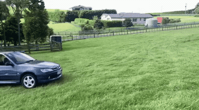 A Car Is Parked In A Grassy Field Next To A Fence . GIF