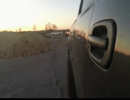 A Car Is Parked On The Side Of The Road With A Sunset In The Background GIF