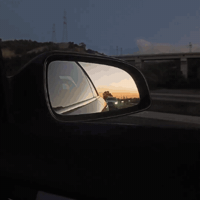 A Car Is Reflected In A Side View Mirror At Sunset GIF