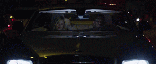 A Car With The Headlights On Is Driving Down A Street At Night GIF