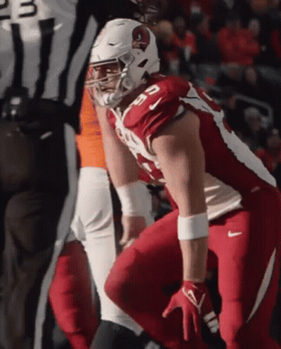 A Cardinals Football Player Squats Down In Front Of A Referee During A Game GIF