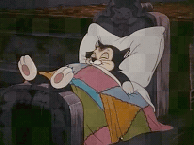 A Cartoon Cat Is Laying In A Bed With A Blanket And Pillow . GIF