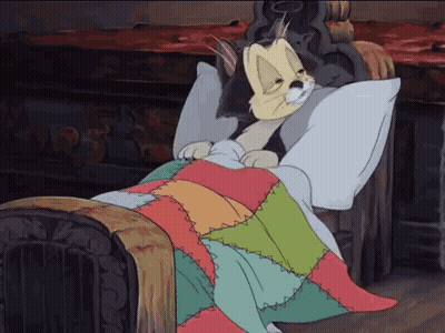A Cartoon Cat Is Laying In A Bed With A Colorful Quilt GIF