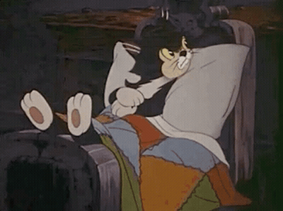 A Cartoon Cat Is Laying In A Bed With A Pillow On Its Head . GIF