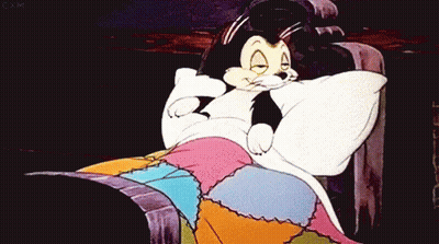 A Cartoon Cat Is Laying In A Bed With A Pillow GIF