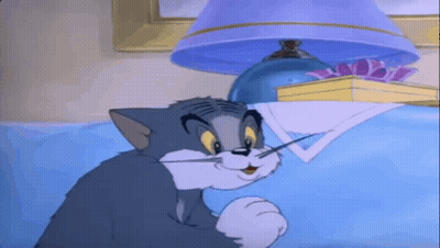 A Cartoon Cat Is Sitting On A Bed Under A Lamp GIF