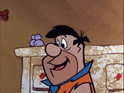 A Cartoon Character From The Flintstones Is Smiling While Standing In Front Of A Fireplace . GIF
