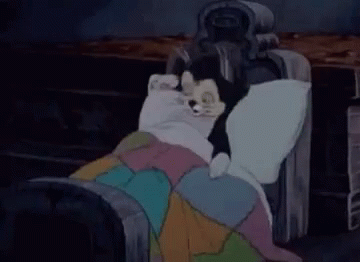 A Cartoon Character Is Laying On A Bed With A Blanket And A Statue . GIF