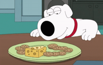 A Cartoon Dog Laying On A Table Looking At A Plate Of Cheese And Cookies GIF