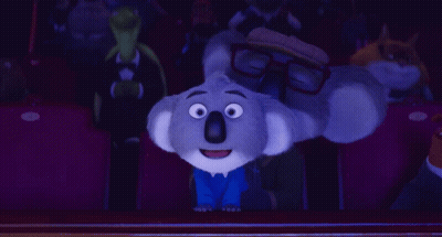 A Cartoon Koala Wearing Glasses Is Sitting In A Theater GIF