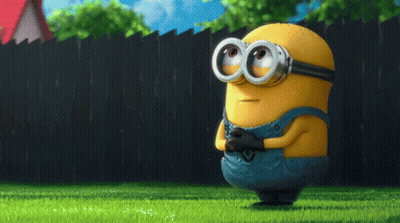 A Cartoon Minion Wearing Goggles And Overalls Stands In The Grass GIF