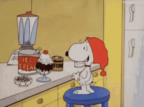 A Cartoon Of Snoopy Sitting On A Stool In Front Of An Ice Cream Sundae In A Kitchen GIF
