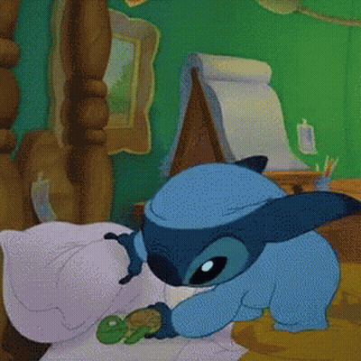 A Cartoon Of Stitch Laying On A Bed GIF