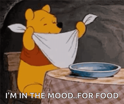 A Cartoon Of Winnie The Pooh Sitting At A Table With A Towel Around His Neck And A Bowl Of Food GIF