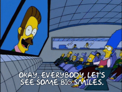 A Cartoon Says Okay Everybody Let 'S See Some Big Smiles In Front Of A Large Screen GIF