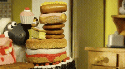A Cartoon Sheep Is Standing Next To A Stack Of Cake And Donuts GIF