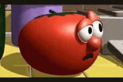 A Cartoon Tomato With Big Eyes And A Big Nose Is Sitting On A Table . GIF
