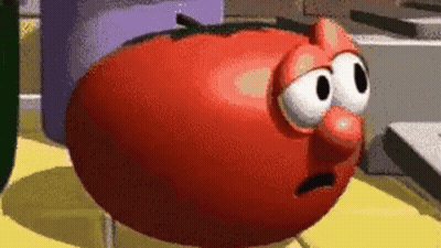 A Cartoon Tomato With Big Eyes And A Red Nose Is Standing On A Table . GIF