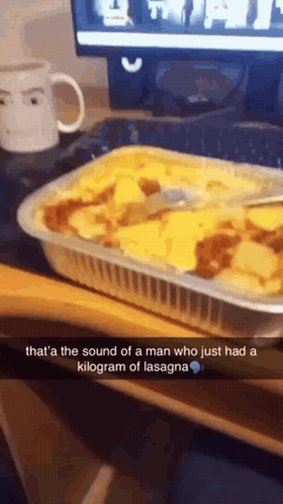 A Casserole Dish Of Lasagna With A Spoon In It On A Desk GIF