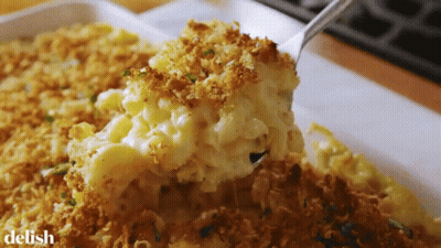 A Casserole Dish With Macaroni And Cheese And A Spoon In It GIF