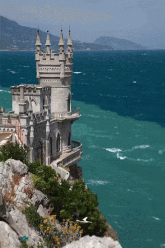 A Castle Sits On A Cliff Overlooking A Body Of Water GIF