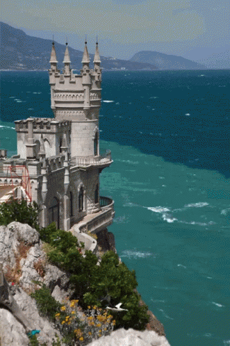 A Castle Sits On A Cliff Overlooking A Body Of Water GIF
