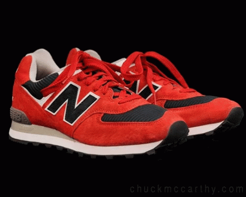 A Cat Sitting On Top Of A Pair Of Red New Balance Shoes GIF