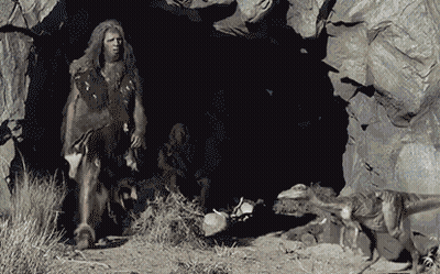 A Caveman Is Standing In Front Of A Cave GIF