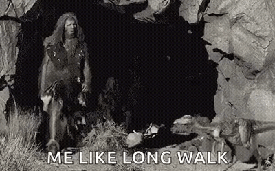 A Caveman Is Walking Through A Cave With A Dog . GIF