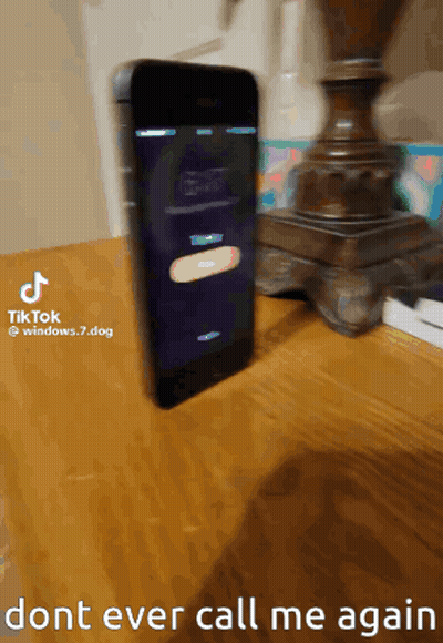 A Cell Phone Is Sitting On A Wooden Table Next To A Lamp And A Sign That Says Do N't Ever Call Me Again GIF